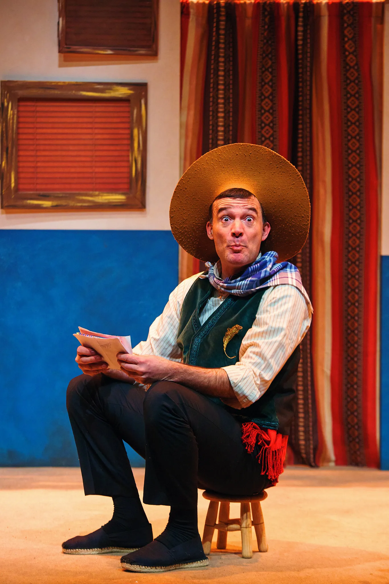 Javier Jiménez con sombrero de paja, sentado en un taburete, lee un papel