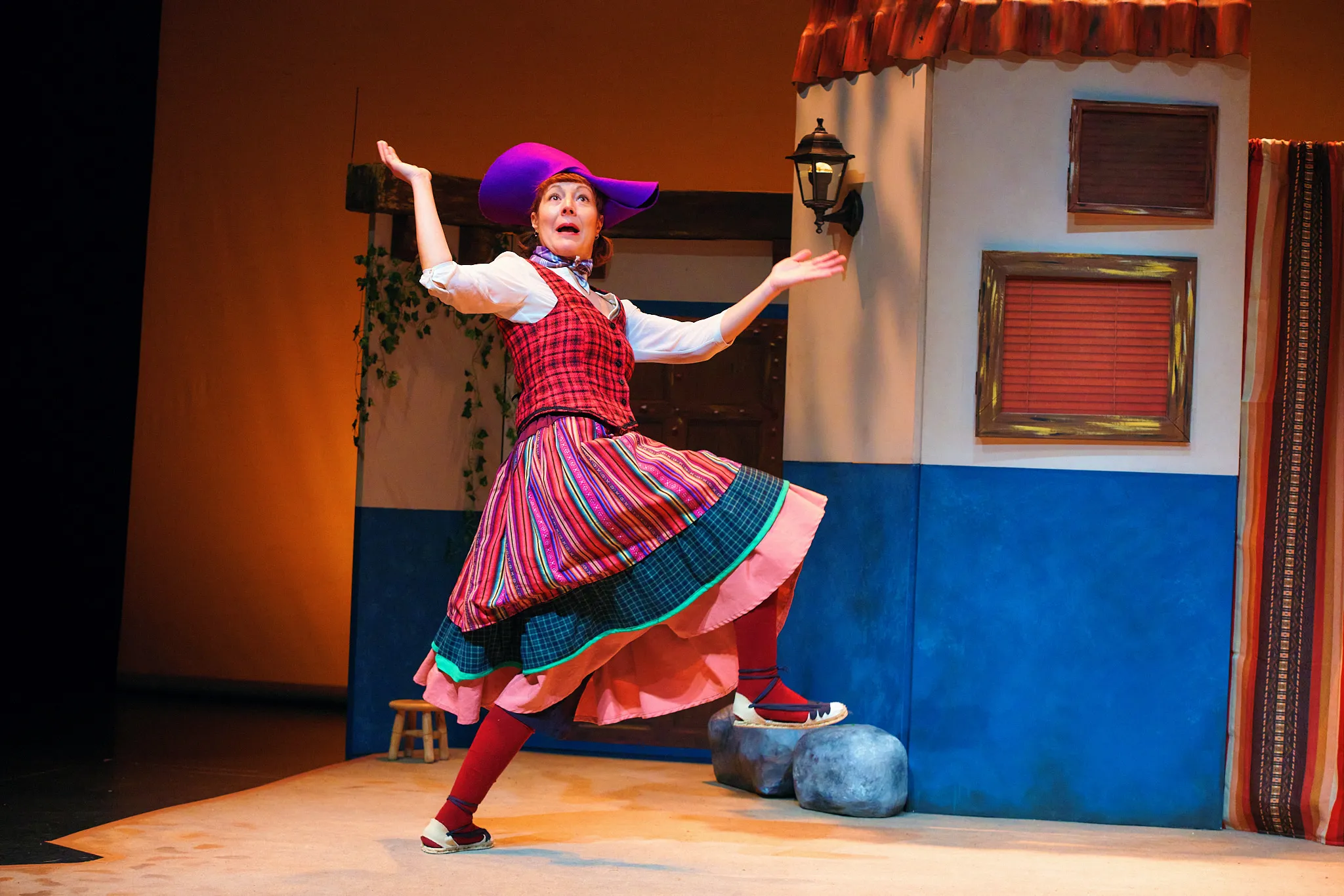 La actriz, con falda de rayas y sombrero morado, baila junto a una casa encalada