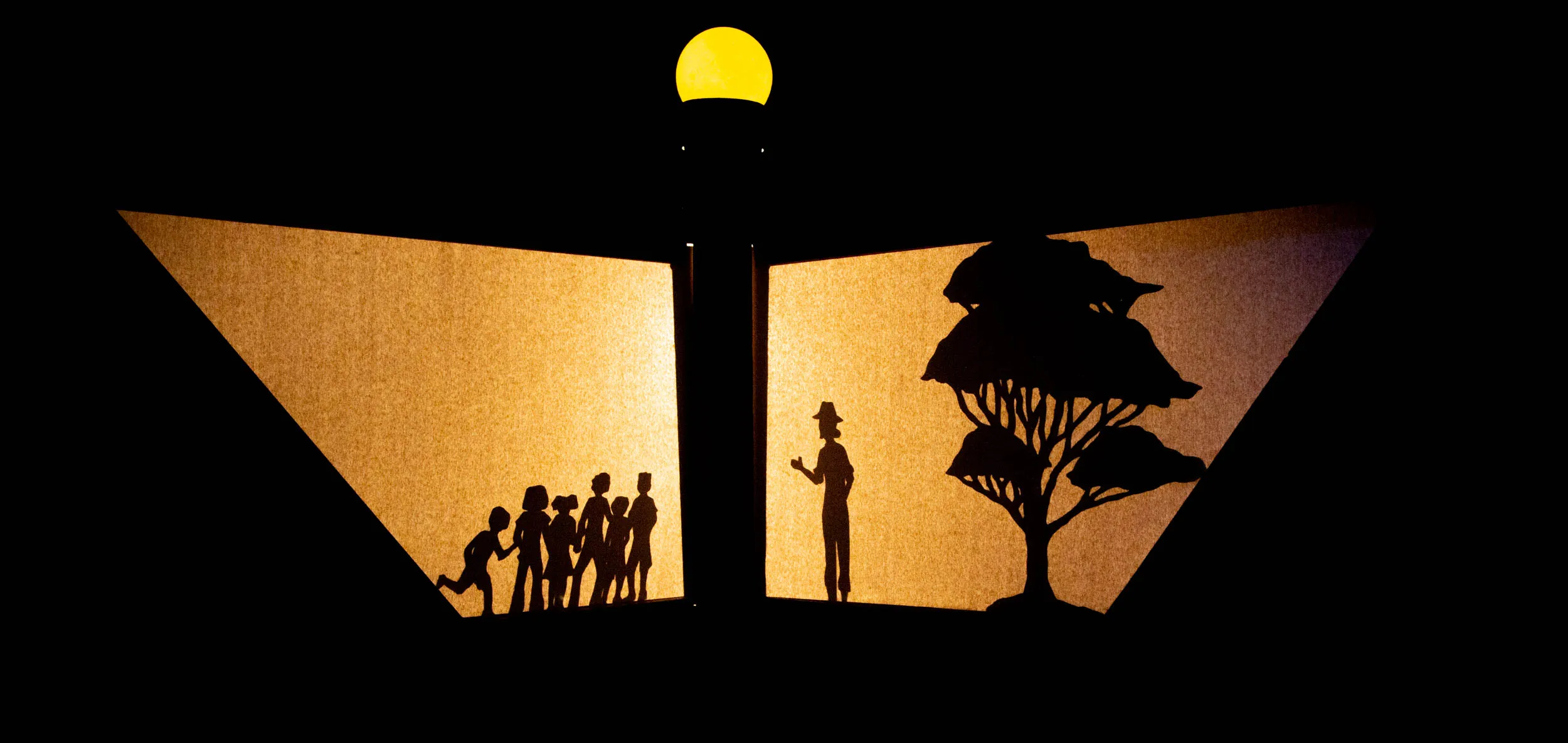 Sombras chinescas de un grupo de personas y un árbol sobre dos pantallas iluminadas